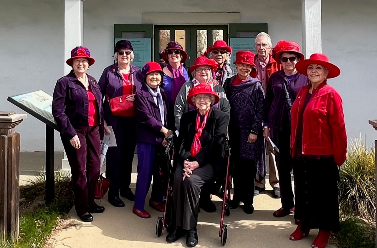 A group of senior ladies in red and purple poses with tour guide outside Alviso Adobe 