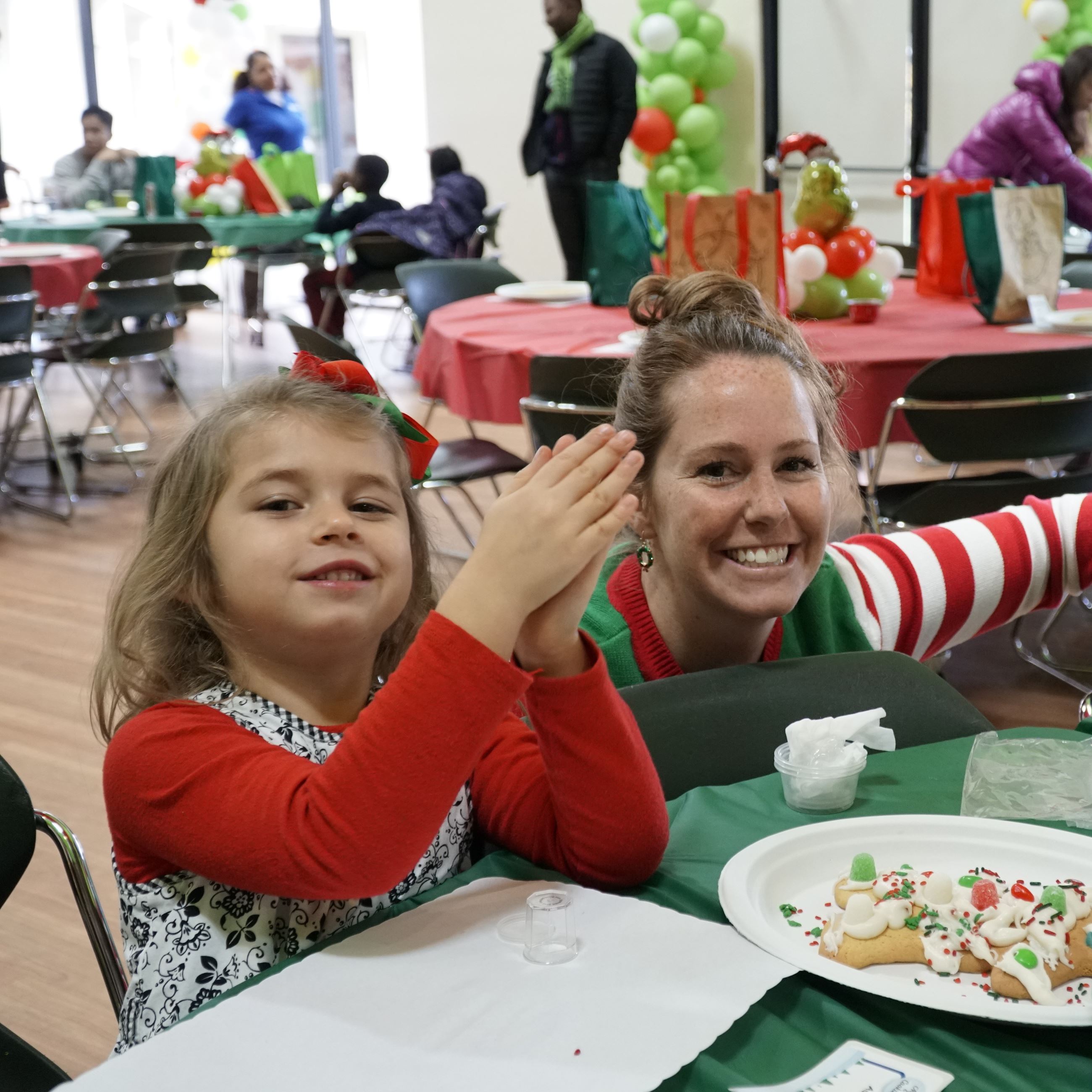 Mom and daughter in festive attire decorating oversize cookie