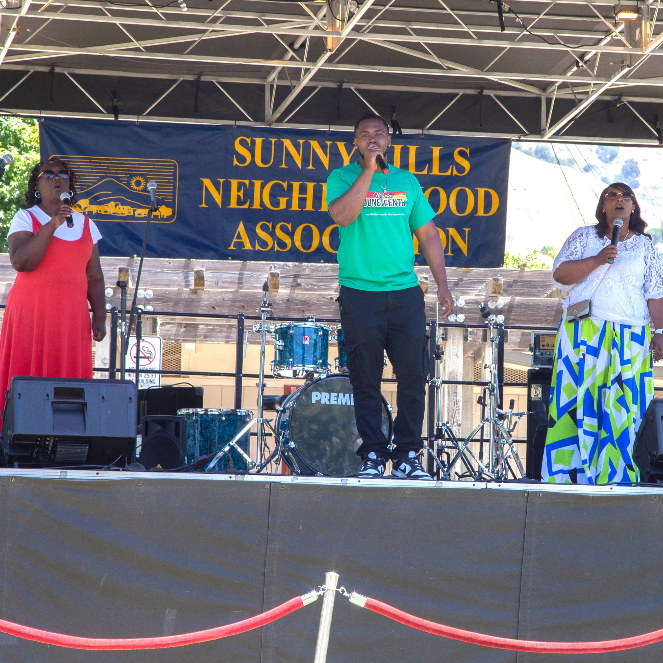Gospel singers perform on a stage in a park.
