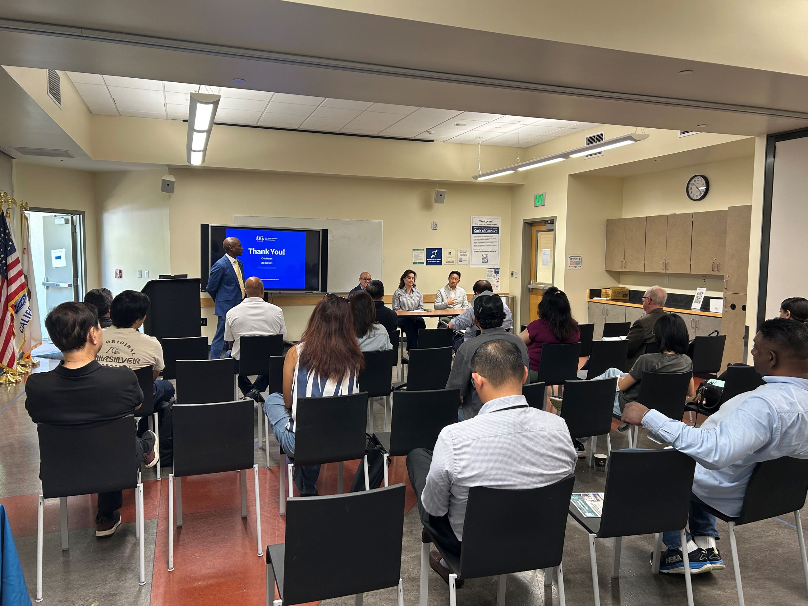 Room of people listening to a lecture.  there is a panel at the front of the room.